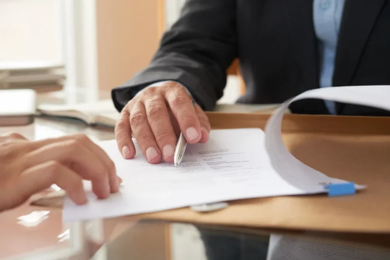 Persona revisando con un bolígrafo un contrato de trabajo junto a otra persona en una mesa de oficina